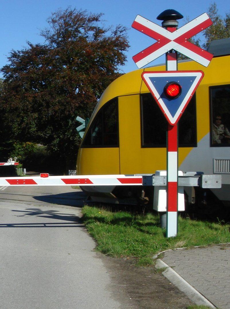 gult lokomotiv kører ind på overkørsel hvoraf den ene bom og vejsignal ses.